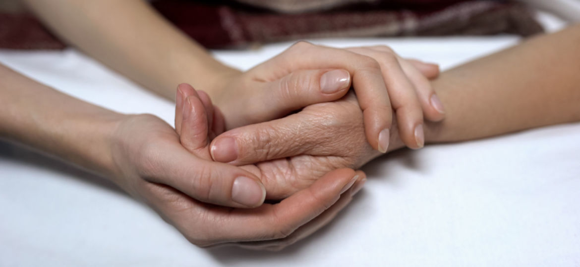 Warm daughters hands holding and calming down sick mother in bed