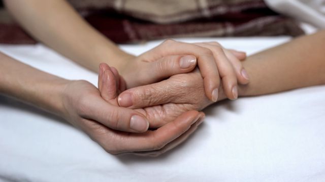 Warm daughters hands holding and calming down sick mother in bed