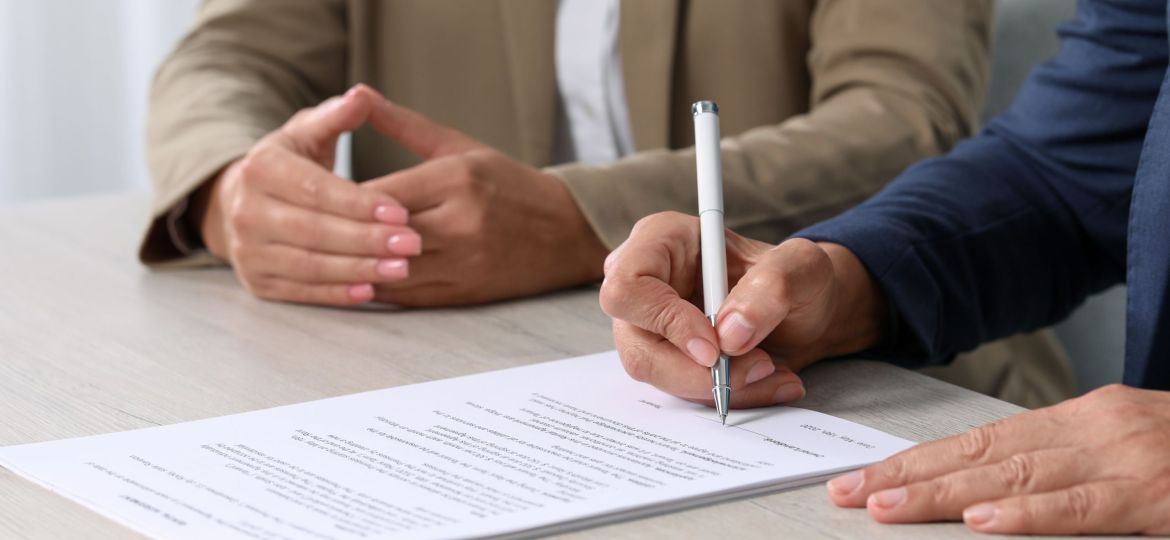 Signing document. Women at light wooden table indoors, closeup