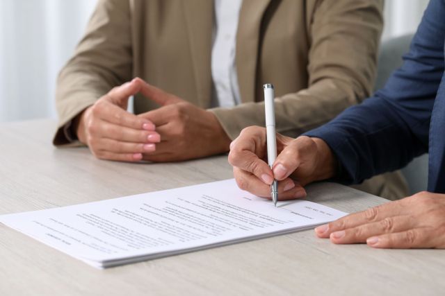 Signing document. Women at light wooden table indoors, closeup